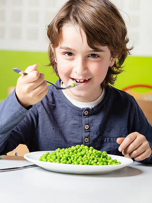 un enfant qui mange à la cantine des petits pois